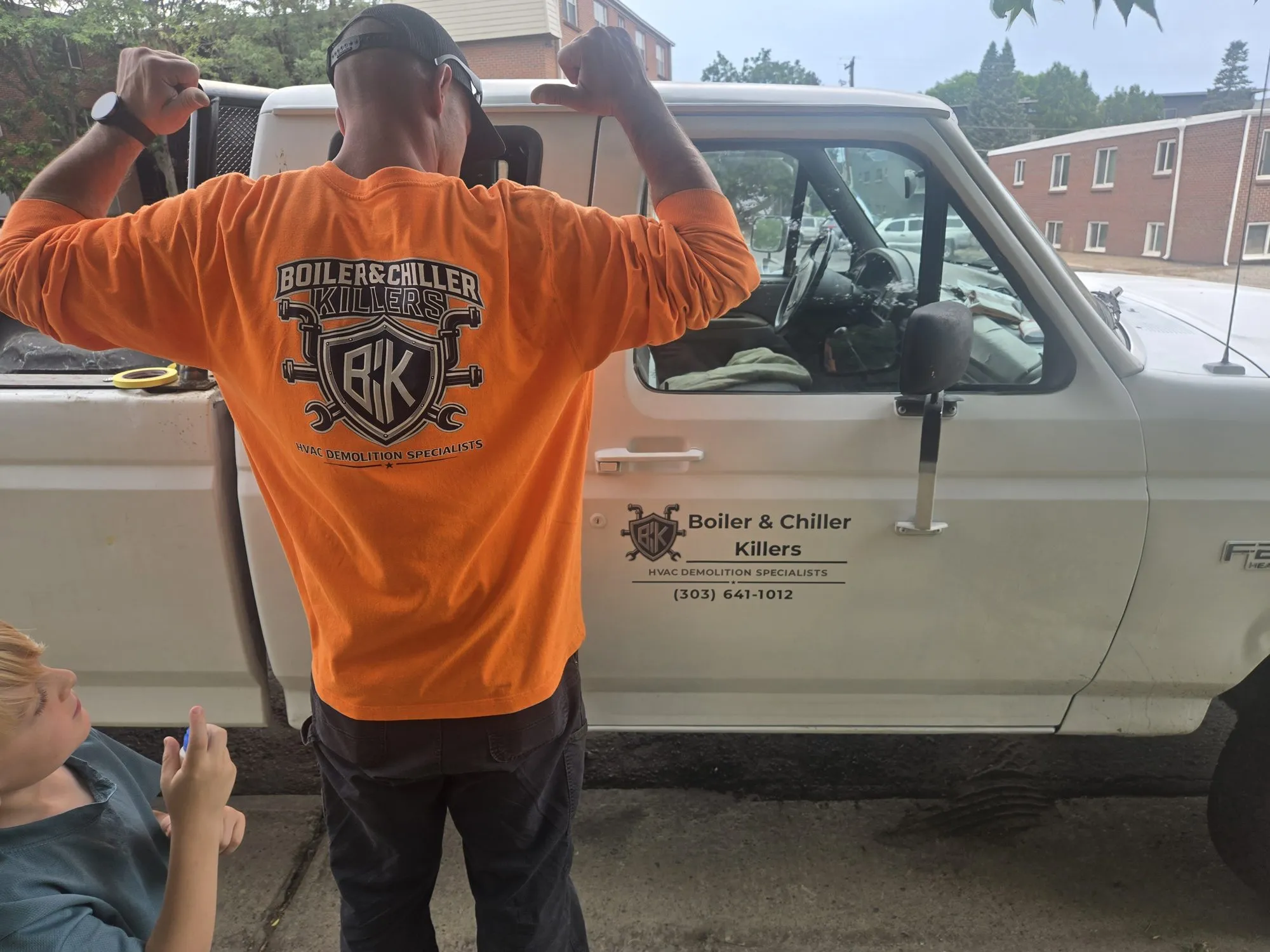 Gadge flexing in a BCK shirt at the work truck while a young family member looks at the logo on his back